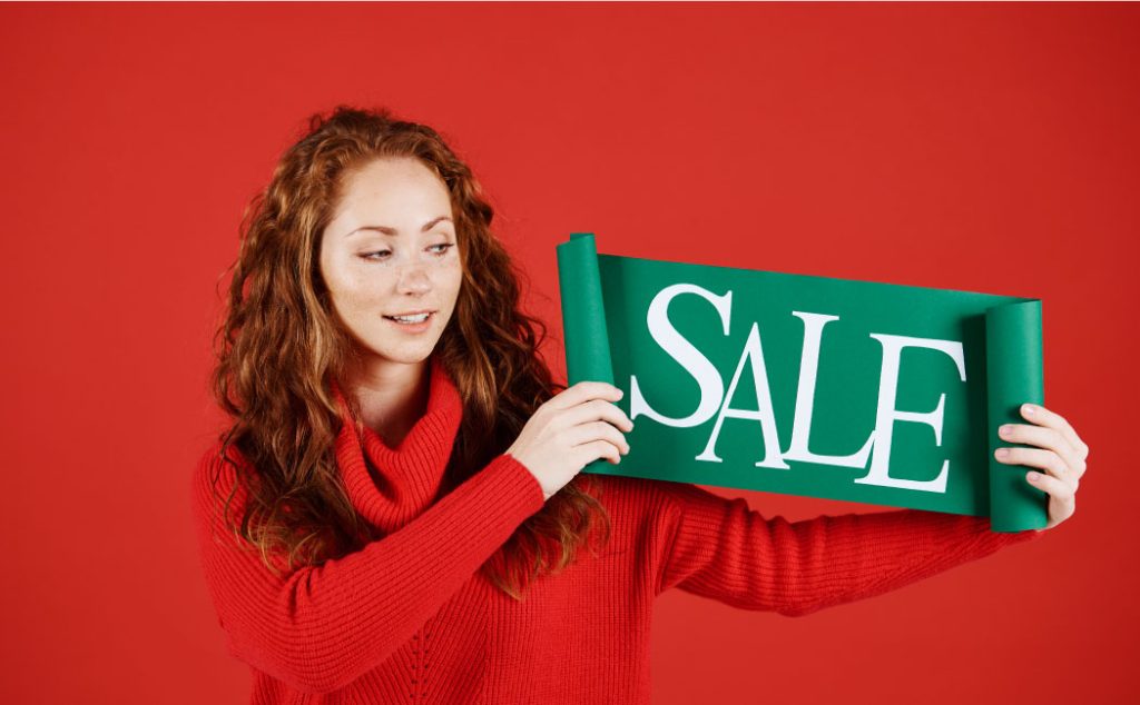 A woman holding a green sign that reads ‘SALE’