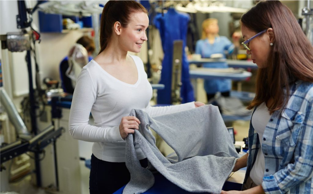 Two women holding a grey piece of fabric in a clothing factory
