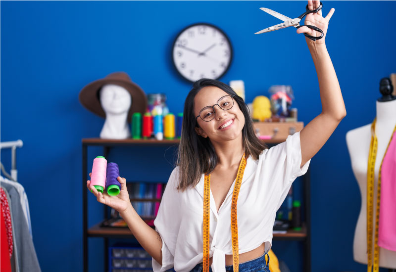 The woman is holding a pair of scissors in one hand and a spool of thread in the other