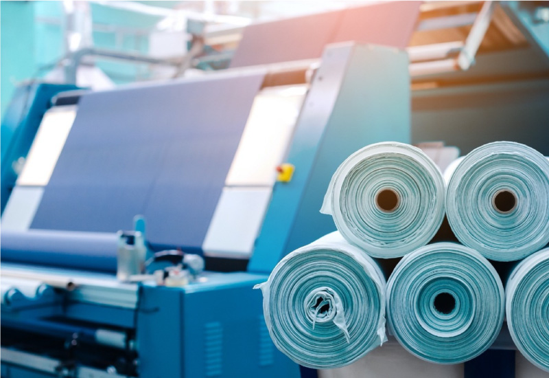 A stack of fabric rolls in front of a machine in a clothing factory