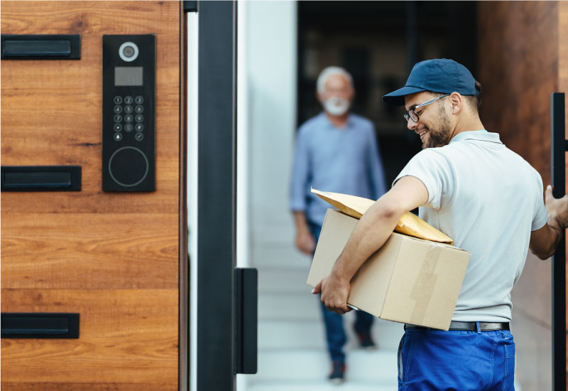 Delivery man holding a package at a door with a blurred person in the background