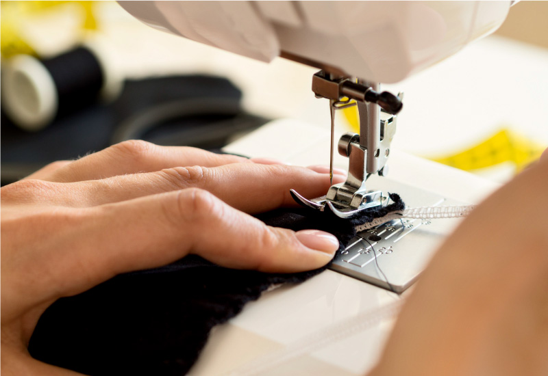  Person sewing black fabric with white thread using a sewing machine.