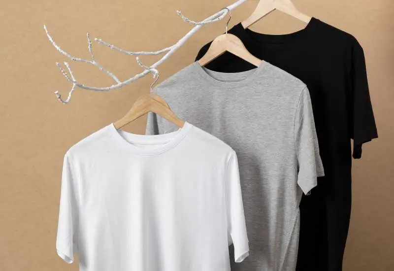 Three t-shirts hanging on a wooden hanger on a branch